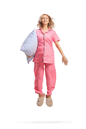 Woman in pajamas holding a pillow and jumping isolated on white backgroundの写真素材