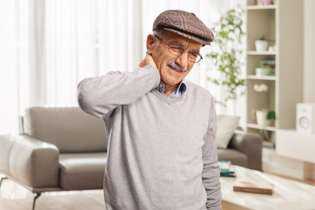 Elderly man with stiff neck standing in a living roomの写真素材