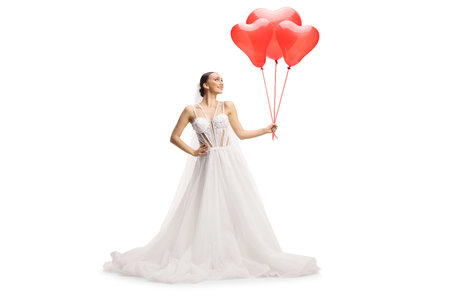 Bride in a white dress holding a bunch od red heart shaped balloons isolated on white backgroundの写真素材
