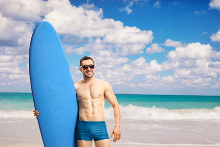 Man in swimwear wearing sunglasses and posing with a surfing board at a beach