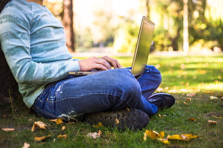 Young man with laptop sitting near lake in city park outdoor