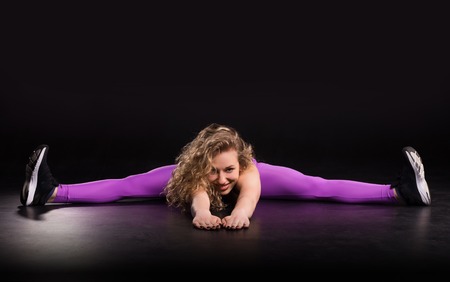 Fitness curly woman training in dark studio. Young girl stretchingの写真素材