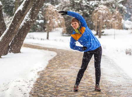 Young sport woman doing exercises during winter training outside in cold snow weather.