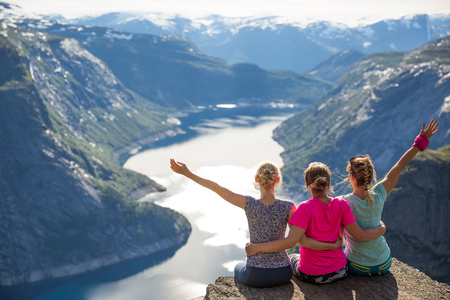 Happy friends relax on Trolltunga. People enjoy beautiful lake and good weatherの写真素材