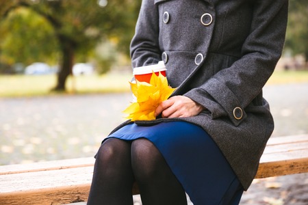 Happy woman in black hat with cup of coffee walking on autumn city park. Rainy weather and yellow trees aroundの写真素材