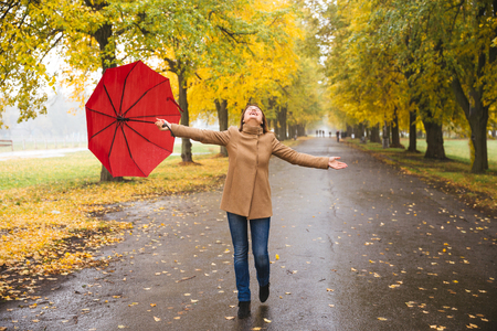 Happy woman with red umbrella walking at the rain in beautiful autumn parkの写真素材