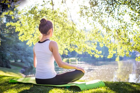 Young woman doing yoga in morning park near lake. Workout at the streetの写真素材
