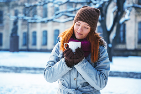 Happy redhead woman walking in winter park and drinking hot coffeeの写真素材