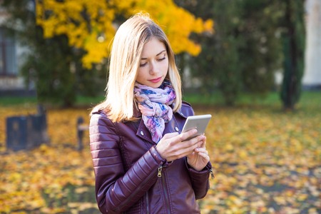 Happy teen girl with phone smile during walking on autumn park. Fall conceptの写真素材