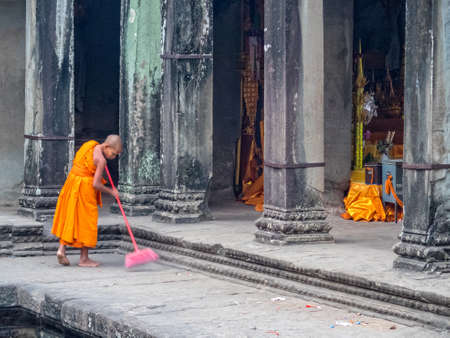 Young monk in orange robe sweeping early morning at Angkor Wat - Siem Reap, Cambodiaのeditorial素材