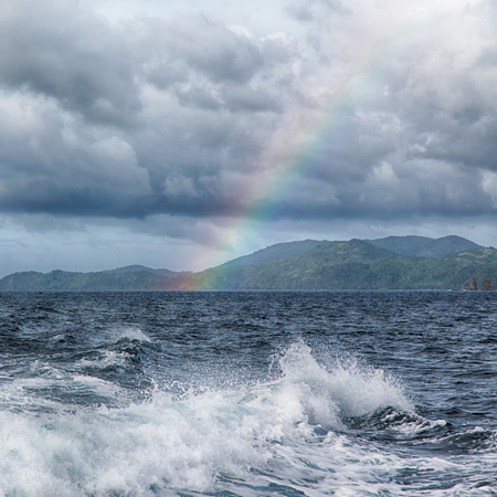 from a boat the rainbow from  ocean and island in backgroundの写真素材