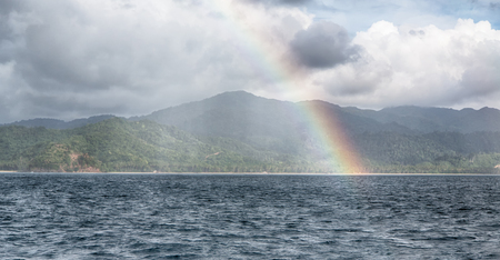 from a boat the rainbow from  ocean and island in backgroundの写真素材