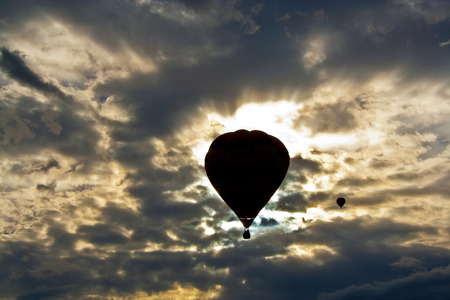 backlit hot air balloon silhouette floating against cumulus grey cloudy skyの写真素材