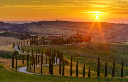 Sunset over the rolling hills, green fields, cypresses trees and winding road in Tuscany, Italyの写真素材