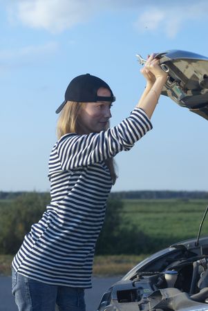 Car on roadside and young woman attempting to repair it
