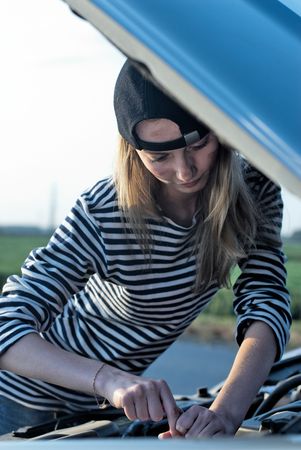 Young woman attemting to repair broken carの写真素材