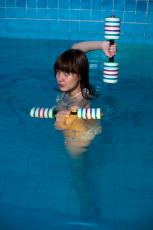 Young beautiful woman doing aqua gym exercise with water dumbbell in a swimming poolの写真素材