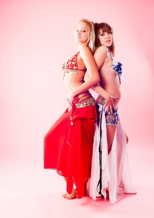 Two beautiful girls in belly dance costume at pink backgroundの写真素材