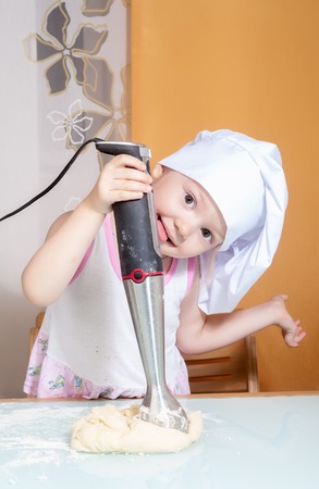 Cute little cook girl stirs dough by blenderの写真素材