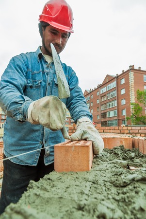 Tyumen, Russia - May 23, 2008: 18 floor residental house at intersection of streets of Gercena and Chelyuskincev. Construction mason worker bricklayer installing red brick with trowel putty knifeのeditorial素材