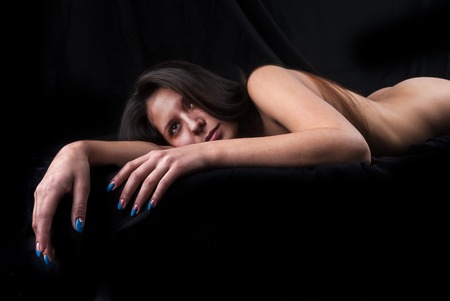 Full-length portrait of beautiful woman lying down on black bed