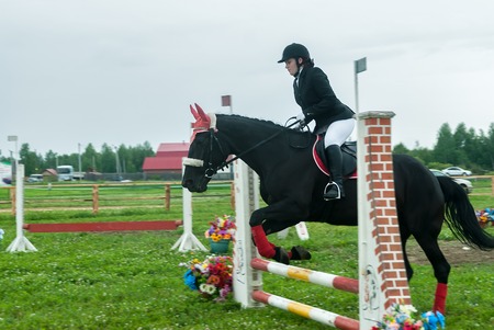 Tyumen, Russia - June 24, 2016: The 5th open championship of Russia on a plowed land. Young girl rider on a horse overcomes obstacles during show programのeditorial素材