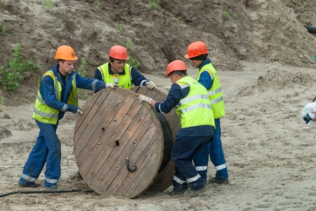 Tobolsk, Russia - July 15. 2016: Sibur company. Construction of plant on processing of hydrocarbons. Workers pulling roll high voltage cable lineのeditorial素材