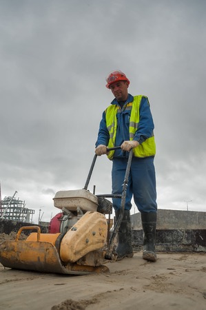Tobolsk, Russia - July 15. 2016: Sibur company. Construction of plant on processing of hydrocarbonic raw materials. Builder worker at sand ground compaction with vibration plate compactor machineのeditorial素材