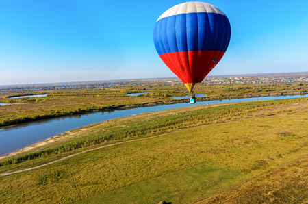 Kaskara, Russia - October 1, 2016: Hot air balloon flying over river landscape at autumn day. Kaskara at background. Tyumen regionの写真素材