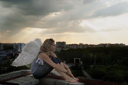 Young beautiful woman with angel wings on building roof looking over cityの写真素材