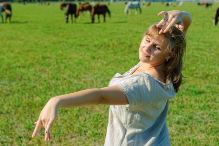 Beautiful woman in traditional dress dances on meadow over horses backgroundの写真素材