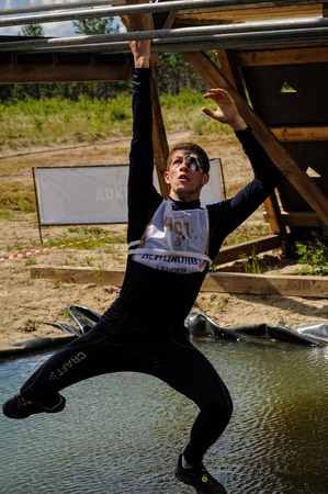 Tyumen, Russia - July 2, 2017: Race of Heroes project on the ground of the highest military and engineering school. The man climbs on bars over waterのeditorial素材