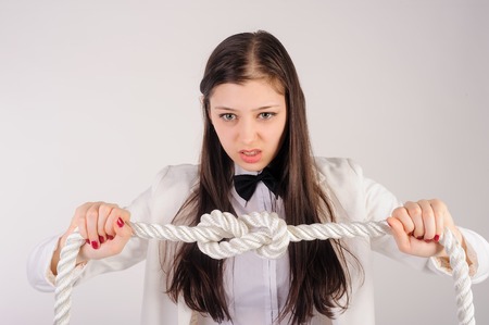 Portrait of pretty angry student or businesswoman thinking that solve a problem to untie knot over white backgroundの写真素材