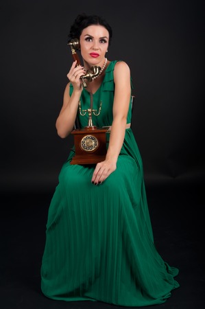 Attractive woman sitting with vintage phone over black backgroundの写真素材