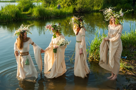 Four attractive women with wreath of flowers enter in lake water. Ivan Kupala Holiday Celebrationの写真素材