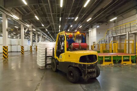 Tobolsk, Russia - July 15. 2016: Sibur company. Polymer plant. Driver on forklift truck loads pallets with finished goods from packaging machine to warehouseのeditorial素材