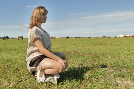 Beautiful woman in traditional dress relaxes on meadow over horses backgroundの写真素材