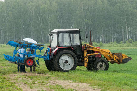 Tyumen, Russia - June 24, 2016: The 5th open championship of Russia on a plowed land. Young operator plows the site on Belarus tractor in rainy weatherのeditorial素材