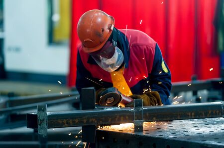 Tyumen, Russia - September 4, 2019: Mostootryad-36 Factory. Heavy industry worker cutting steel pipe with angle grinder in workshopのeditorial素材