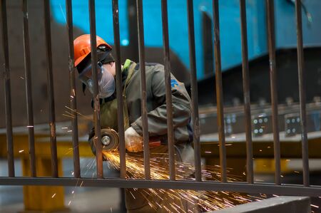 Tyumen, Russia - September 4, 2019: Mostootryad-36 Factory. Heavy industry worker cutting steel pipe with angle grinder in workshopのeditorial素材