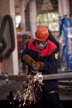 Tyumen, Russia - September 4, 2019: Mostootryad-36 Factory. Heavy industry worker cutting steel pipe with angle grinder in workshopのeditorial素材