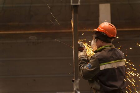Tyumen, Russia - September 4, 2019: Mostootryad-36 Factory. Heavy industry worker cutting steel pipe with angle grinder in workshopのeditorial素材