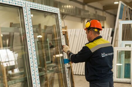 Tyumen, Russia - September 4, 2019: Workshop of Mostootryad-36 Factory for aluminum and PVC windows and doors production. Manual worker assembling PVC window with screw gunのeditorial素材