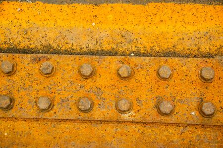 Antique rusty metal square nuts locked with rust and corrosion on old heavy duty bolts holding a thick and corroded vintage industrial steel plate structure as a retro grunge backgroundの写真素材
