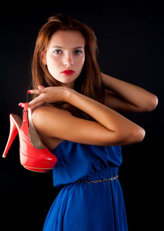 Attractive cool redhaired woman holding red shoes on blackの写真素材