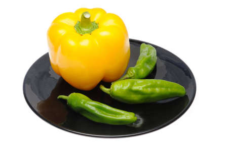 Yellow and green peppers on black dish isolated over white background