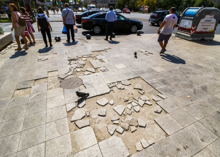 Bucharest, Romania - August 28, 2019: People walks on the sidewalk full of pits in front of the Unirea Shopping Center, the busiest place in Bucharest. This image is for editorial use only.のeditorial素材