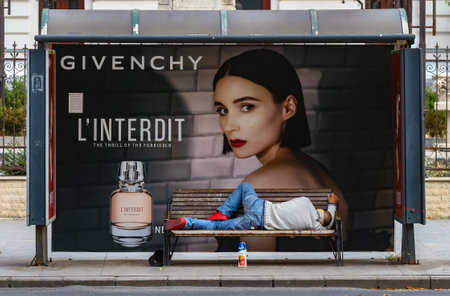 Bucharest, Romania - September 18, 2019: An man looking like a homeless is sleeping on University bus station bench in front of a Givenchy commercial in downtown Bucharest. For editorial use only.のeditorial素材