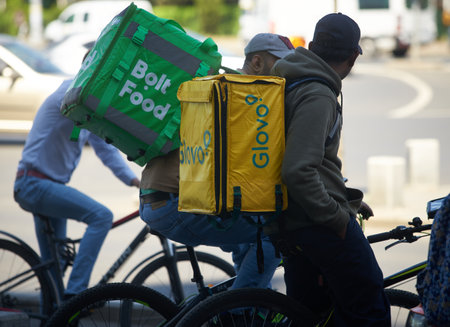 Bucharest, Romania - 2st May, 2023: Two Bolt Food and Glovo food delivery couriers, workers of foreign origin, most likely from South Asia, delivers food in Bucharest, Romania.のeditorial素材