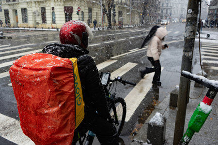 Bucharest, Romania - 7th Dec, 2023: A Glovo food delivery courier, delivers food during the first snowfall in Bucharest, Romania.のeditorial素材